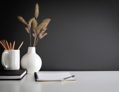 A clean and modern office workspace featuring a pen holder, notebook, and ceramic vase against a