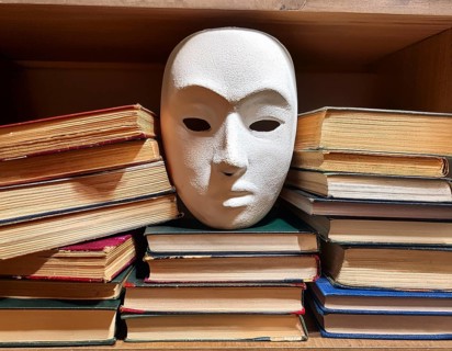 An artistic arrangement featuring a white theatrical mask placed amid various open old books,