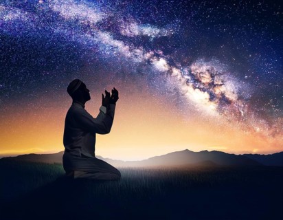 A man kneels in peaceful reflection under the vibrant Milky Way galaxy at sunset in an open natural