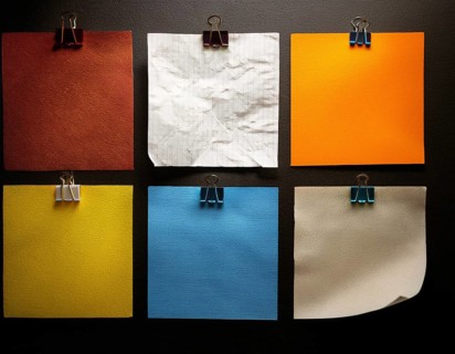 An arrangement of colorful square paper sheets held by binder clips, placed on a dark surface,
