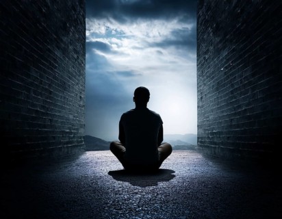 Silhouette of a person sitting alone within a brick archway, observing a peaceful and scenic cloudy
