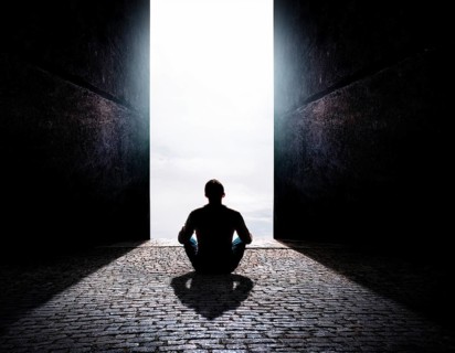 Silhouette of a person sitting alone within a brick archway, observing a peaceful and scenic cloudy