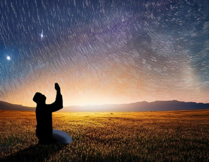 A man kneels in peaceful reflection under the vibrant Milky Way galaxy at sunset in an open natural
