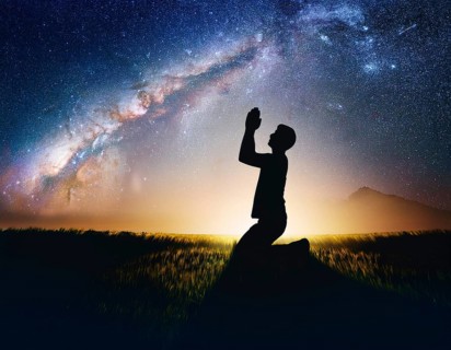A man kneels in peaceful reflection under the vibrant Milky Way galaxy at sunset in an open natural