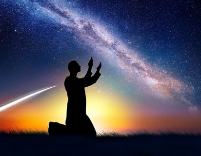 A man kneels in peaceful reflection under the vibrant Milky Way galaxy at sunset in an open natural