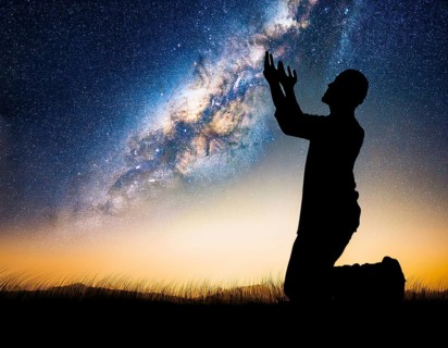 A man kneels in peaceful reflection under the vibrant Milky Way galaxy at sunset in an open natural