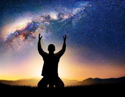 A man kneels in peaceful reflection under the vibrant Milky Way galaxy at sunset in an open natural