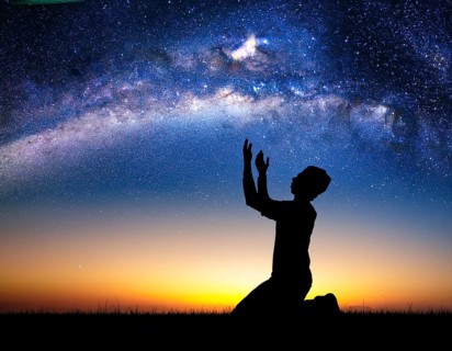 A man kneels in peaceful reflection under the vibrant Milky Way galaxy at sunset in an open natural