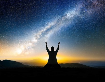 A man kneels in peaceful reflection under the vibrant Milky Way galaxy at sunset in an open natural