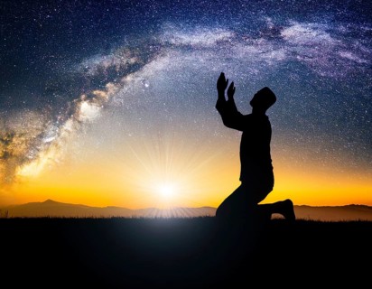 A man kneels in peaceful reflection under the vibrant Milky Way galaxy at sunset in an open natural