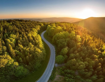A scenic aerial view of a serpentine road surrounded by lush green forest, illuminated by soft