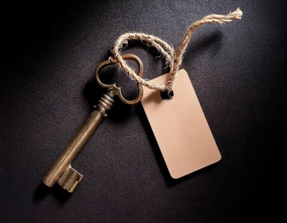 A close-up of an ornate vintage key with a blank label attached, resting on a brown surface under