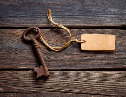 A close-up of an ornate vintage key with a blank label attached, resting on a brown surface under