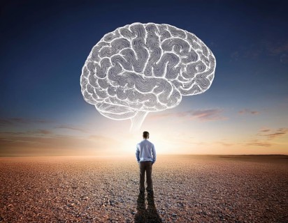 A lone figure stands before a giant brain floating in a surreal desert setting, symbolizing