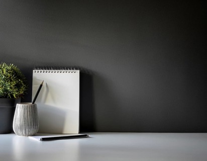 A clean and modern office workspace featuring a pen holder, notebook, and ceramic vase against a