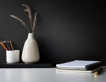 A clean and modern office workspace featuring a pen holder, notebook, and ceramic vase against a