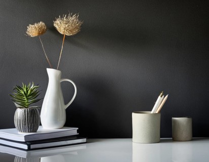 A clean and modern office workspace featuring a pen holder, notebook, and ceramic vase against a