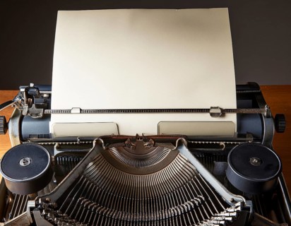 View from above of a retro typewriter equipped with a blank paper sheet, representing creativity,