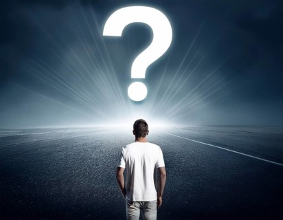 A person stands in contemplation near a large glowing question mark on an open grassy plain,