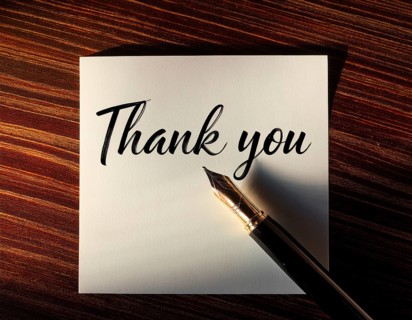 Elegant pen rests alongside a handwritten Thank You card on a wooden surface in soft light.