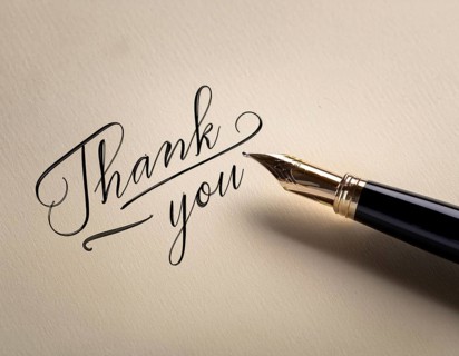 Elegant pen rests alongside a handwritten Thank You card on a wooden surface in soft light.