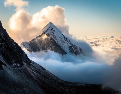 A stunning view of a snowy mountain peak rising above the clouds, with a blue sky background.