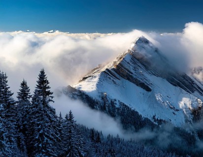 A stunning view of a snowy mountain peak rising above the clouds, with a blue sky background.