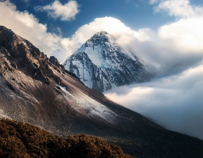 A stunning view of a snowy mountain peak rising above the clouds, with a blue sky background.