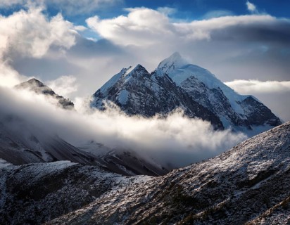 A stunning view of a snowy mountain peak rising above the clouds, with a blue sky background.