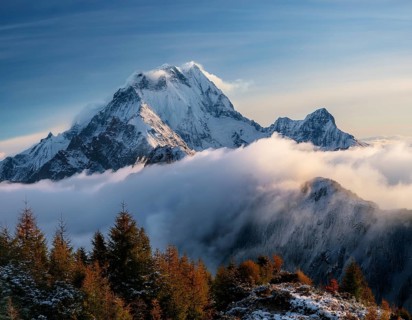 A stunning view of a snowy mountain peak rising above the clouds, with a blue sky background.
