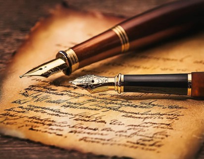 Close-up of a classic fountain pen lying atop old aged paper on a wooden surface, symbolizing