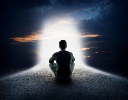 An individual sits in quiet contemplation near the ocean during sunset, surrounded by dramatic