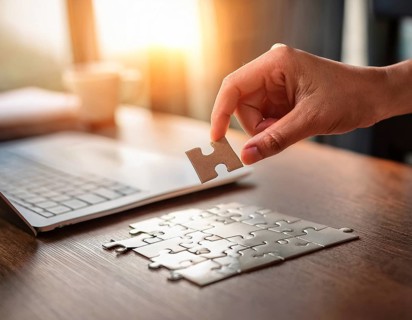 A person's hand placing a puzzle piece on a reflective surface in an office setting as the sun