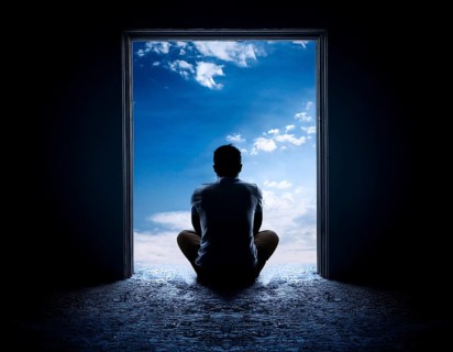 Silhouette of a person sitting alone within a brick archway, observing a peaceful and scenic cloudy