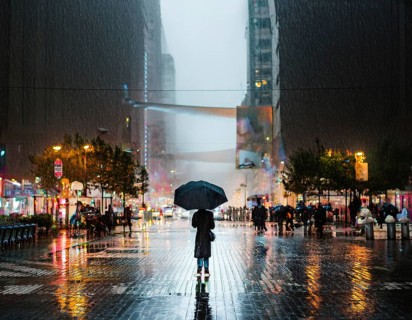 A solitary figure with an umbrella stands amidst a bustling city illuminated by lights, with