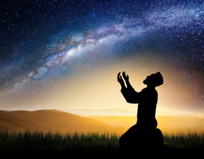 A man kneels in peaceful reflection under the vibrant Milky Way galaxy at sunset in an open natural