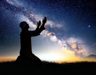 A man kneels in peaceful reflection under the vibrant Milky Way galaxy at sunset in an open natural