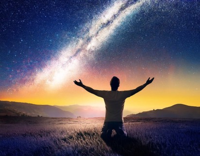 A man kneels in peaceful reflection under the vibrant Milky Way galaxy at sunset in an open natural
