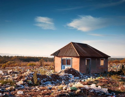 An abandoned house sits amidst scattered garbage in a deserted rural area, conveying environmental