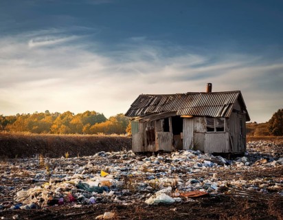 An abandoned house sits amidst scattered garbage in a deserted rural area, conveying environmental