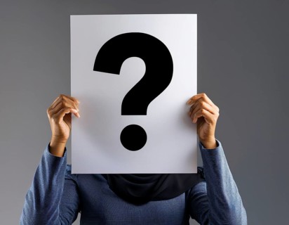 A person concealing their face while holding a question mark sign, symbolizing anonymity, mystery,