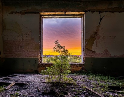 An abandoned building reveals a stunning view of a colorful sunset through a decayed window,