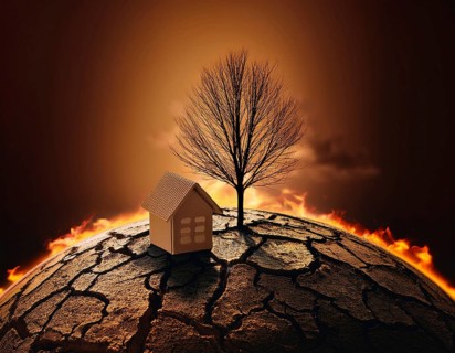 A miniature house and bare tree on cracked soil with a vivid orange sunset, symbolizing