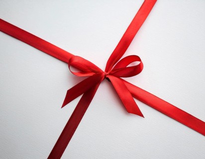 A beautifully wrapped gift box adorned with red satin ribbons forming a bow, contrasting against a