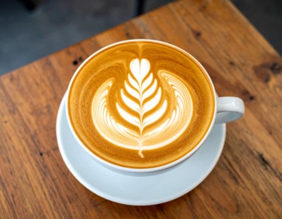 A cozy café latte with heart foam art on wooden table, representing comfort, relaxation, and warm
