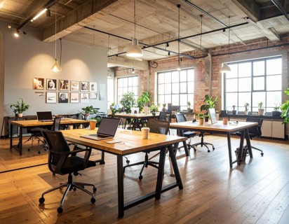Modern coworking space with laptops, coffee cups, plants, and daylight showcasing minimal interior