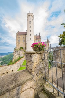A tall tower with pink flowers in a stone wall arrangement in front of a castle, Lichtenstein