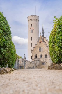 Majestic castle with towers and manicured hedges, captured from a view along a cobbled path,