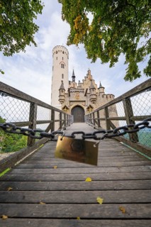 A bridge leads to a majestic Gothic-style castle surrounded by autumnal trees, Lichtenstein Castle,