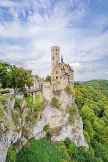 Medieval castle with high tower on a rocky outcrop surrounded by lush green forests and dramatic